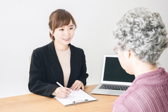 窓口で申請書の記入を手伝うスタッフと高齢の利用者