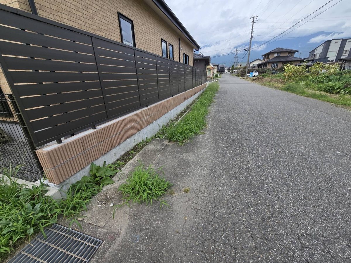 駒ヶ根市の道路縁の草刈り前:フェンス基礎沿いに雑草が茂る状態